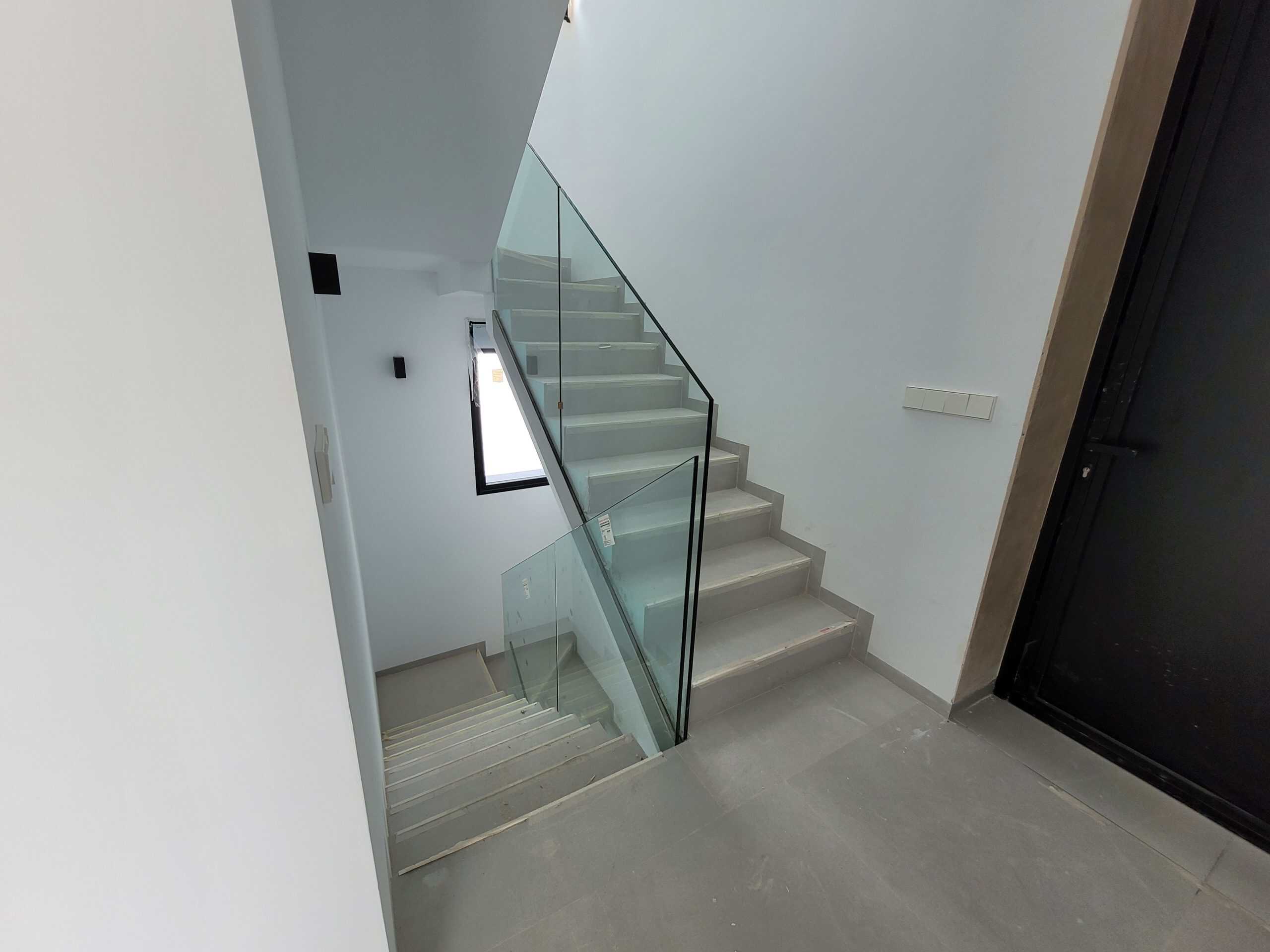 Strakke glazen trap en moderne trapleuning in nieuwbouw woning.