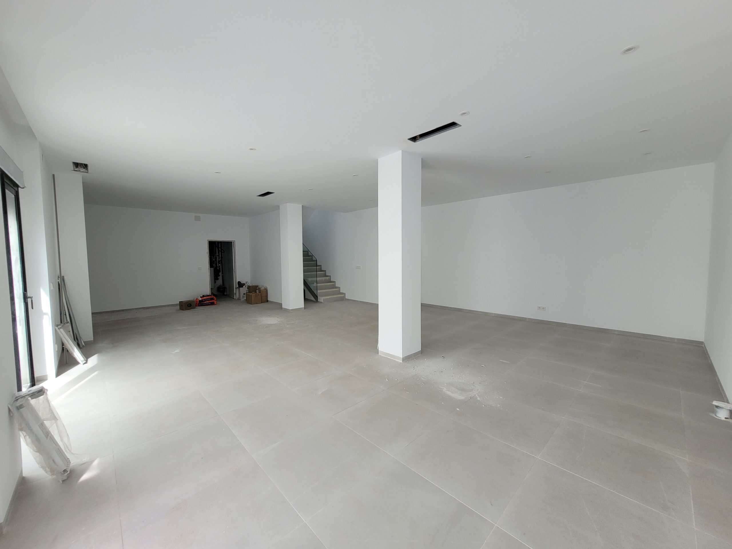 Ruim, ongerealiseerde woonkamer met witte muren en grote ramen, klaar voor afwerking en inrichting.