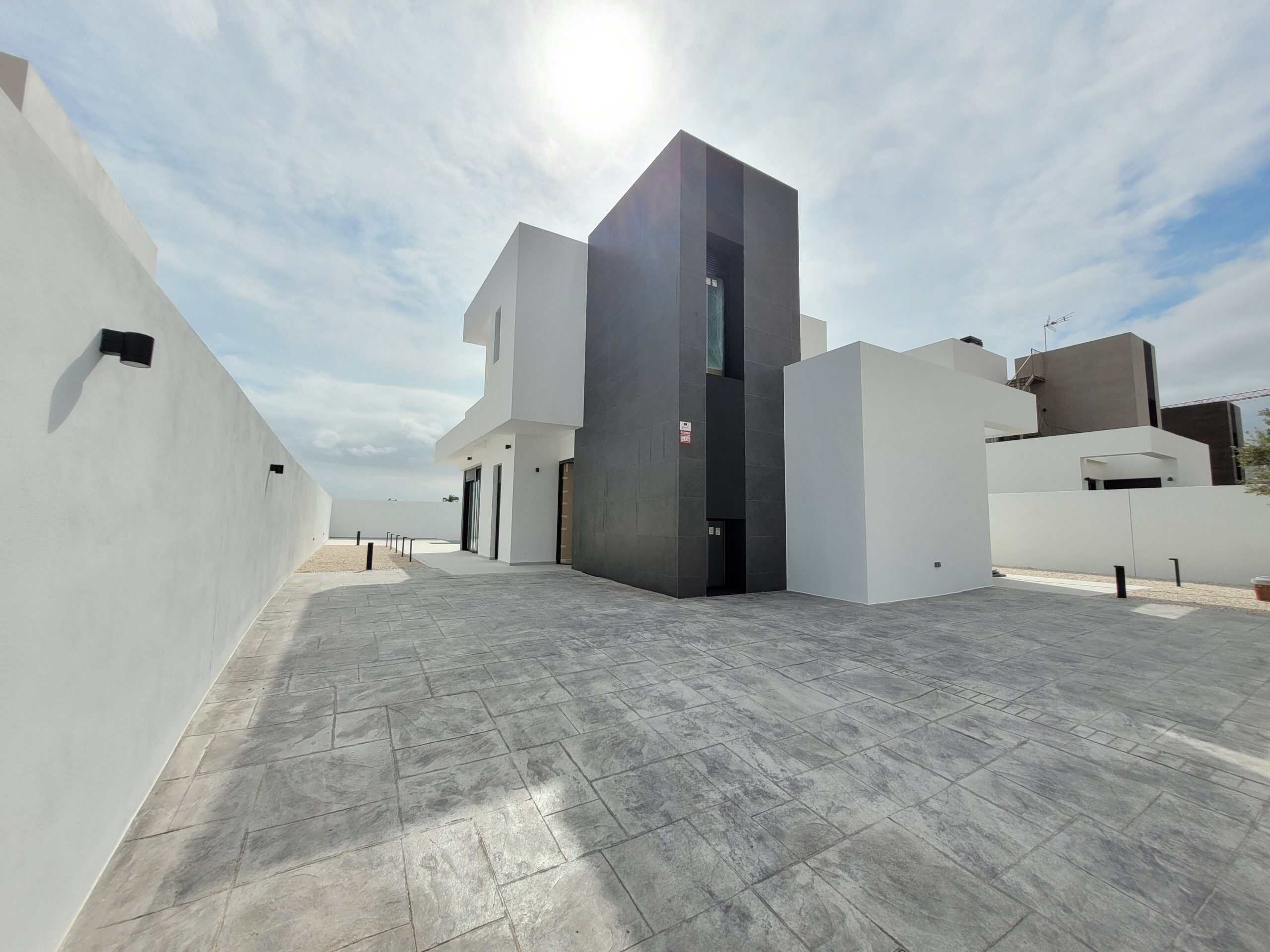 Moderne woning met strakke witte en donkere gevels, ruime betegelde buitenruimte en minimalistisch architectuur.