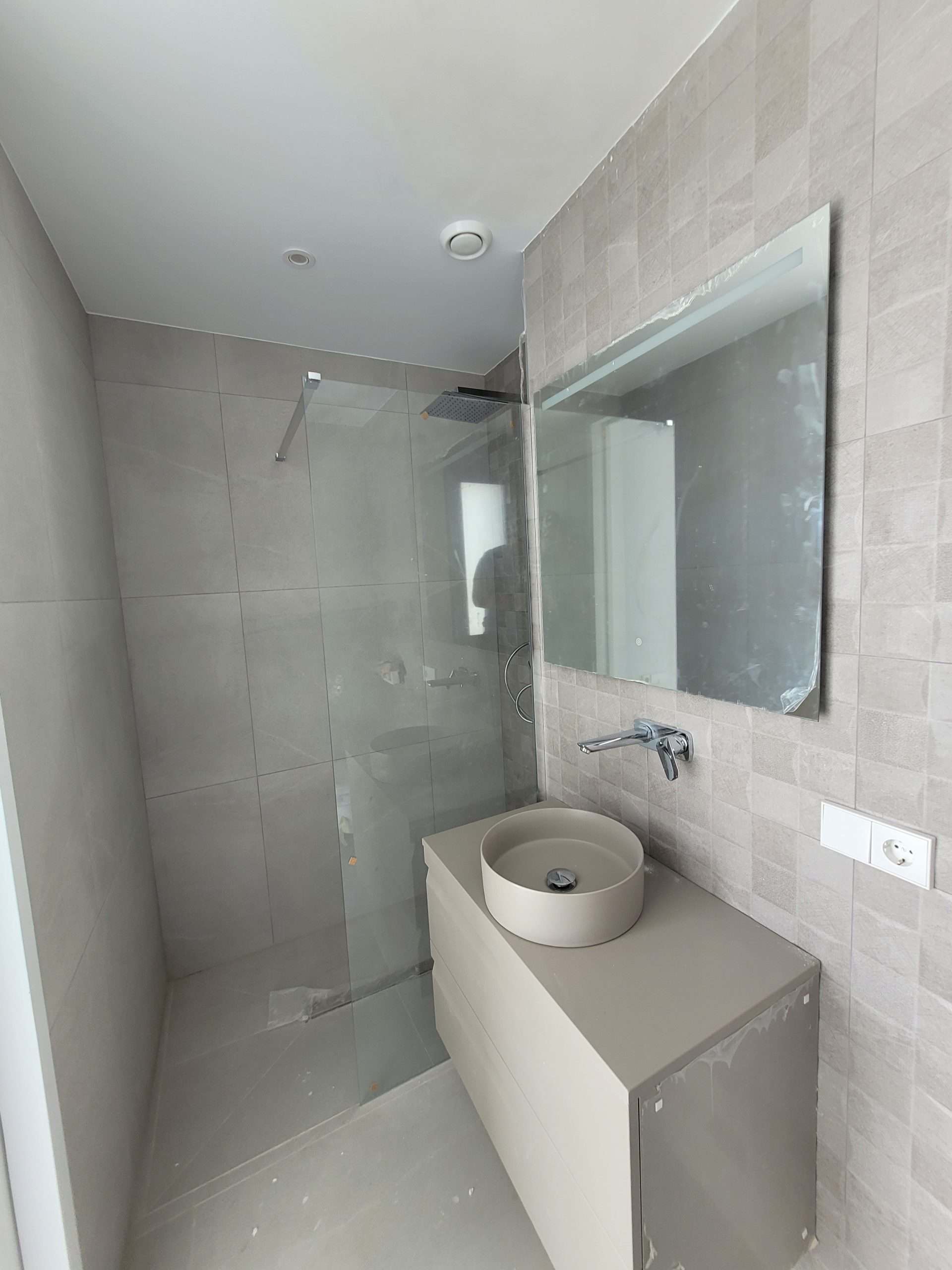 Moderne badkamer met inloopdouche, ronde wastafel en spiegel, afgewerkt met natuurlijke tinten en sleek design.