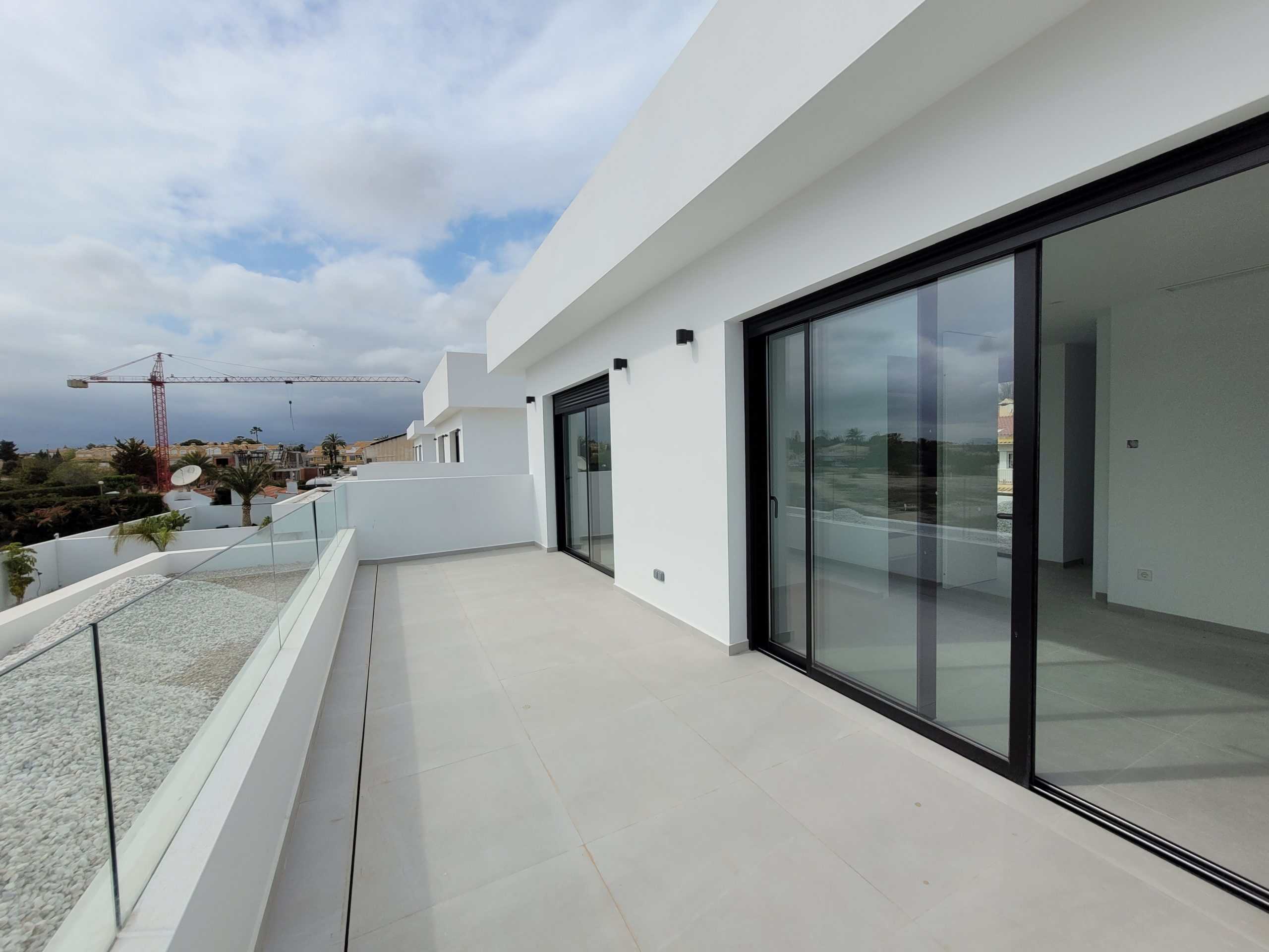 Moderne witte balkon met glasbalustrade en grote glazen schuifdeuren op een nieuwbouwwoning.