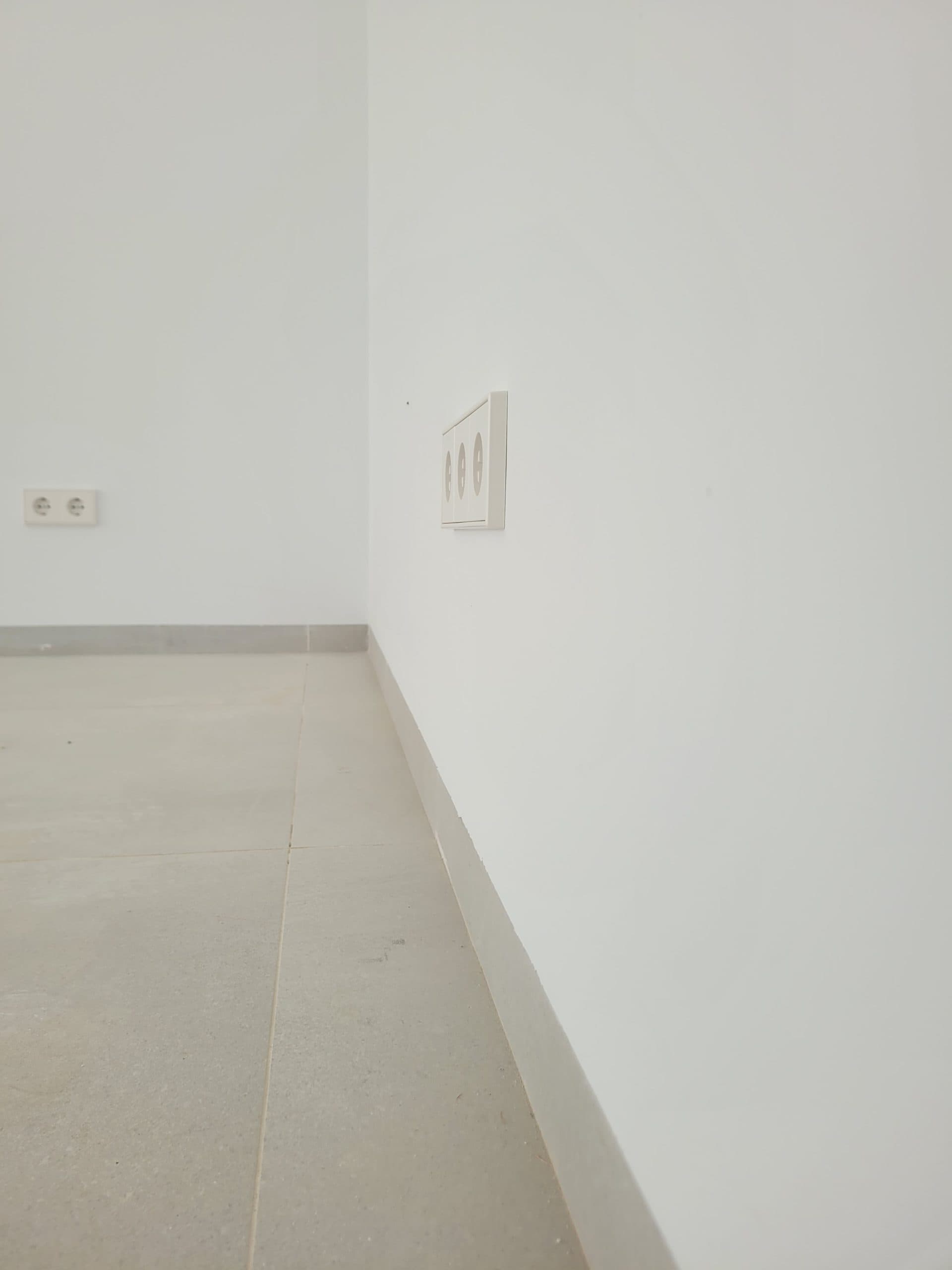 Onbekende witte wand met elektrische stopcontacten en vloer in moderne interieurstijl.
