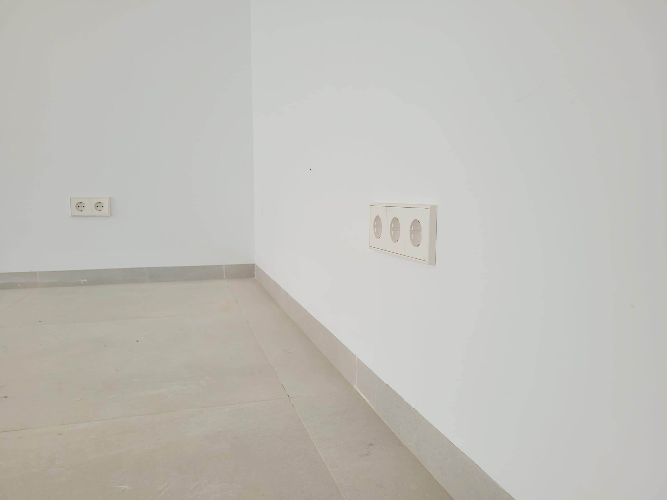 Witte wand met elektrische en netwerkdozen in een nieuw afgewerkt interieur.