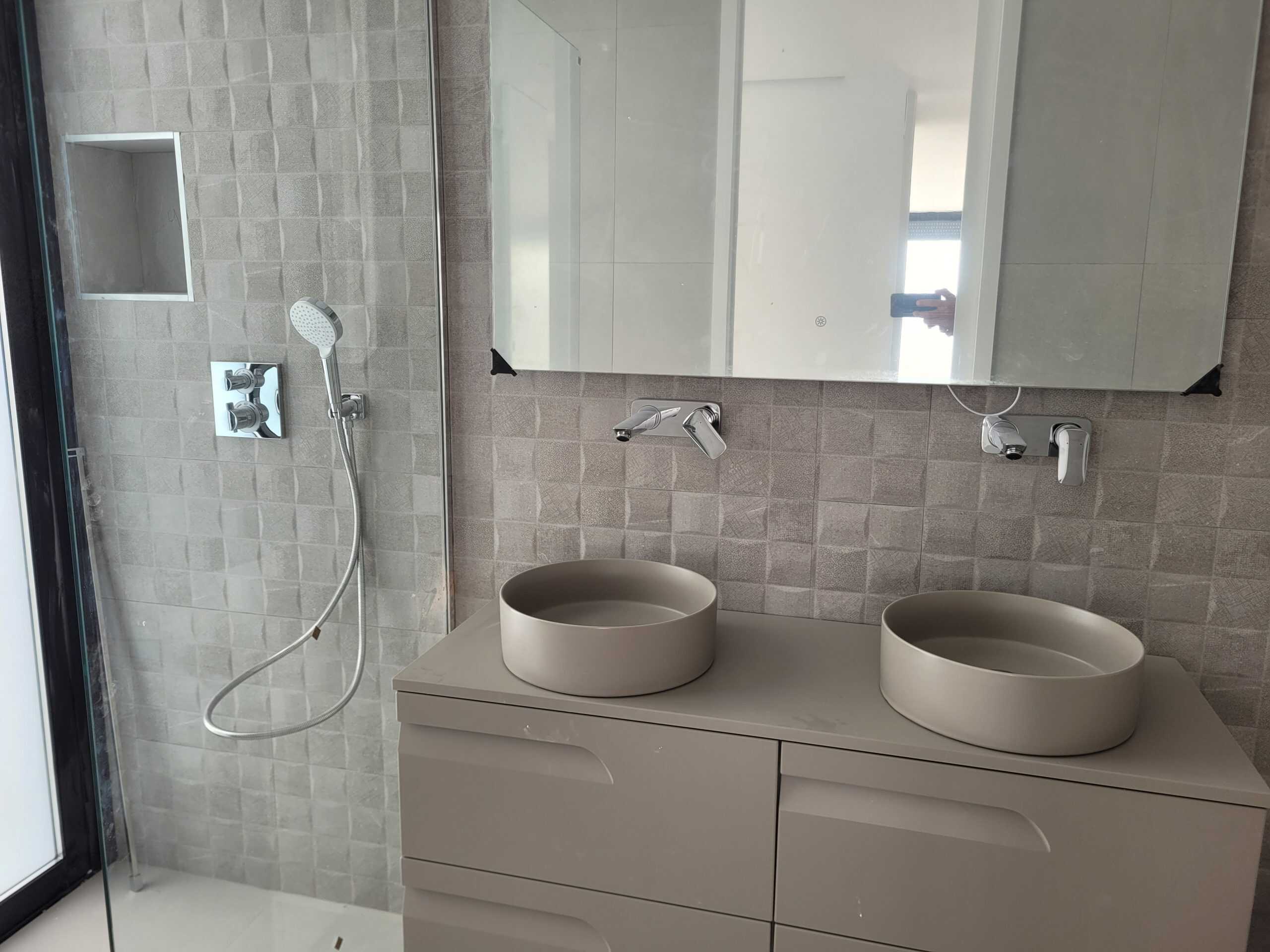 Zweeds badkamer met moderne inloopdouche en dubbele wastafel, strakke design en neutrale kleuren voor een rustige uitstraling.